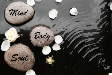 Spa stones with words Mind, Body, Soul and rose petals in water, flat lay. Zen lifestyle