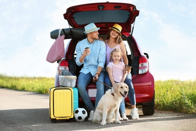 Young family with luggage and dog near car trunk outdoors