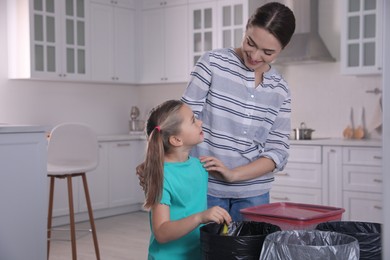 Young woman and her daughter throwing banana peel into trash bin in kitchen. Separate waste collection