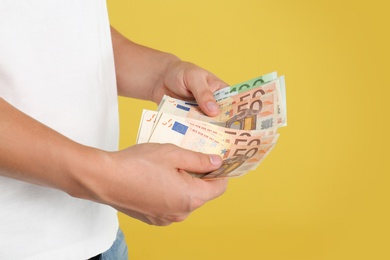 Man with Euro banknotes on yellow background, closeup