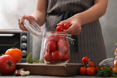 Woman putting tomatoes into glass jar at kitchen table, closeup. Pickling vegetables