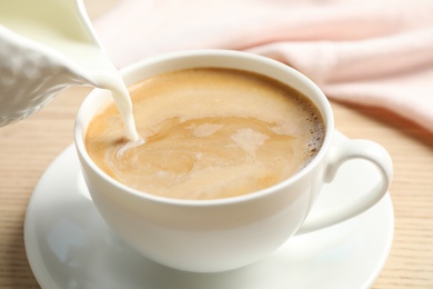 Pouring milk into cup of hot coffee on wooden table, closeup