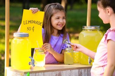 Cute little girl selling natural lemonade to kid in park. Summer refreshing drink