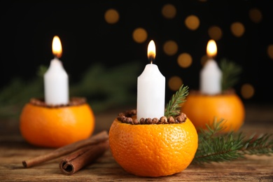 Photo of Burning candle in tangerine peel as holder on wooden table against black background