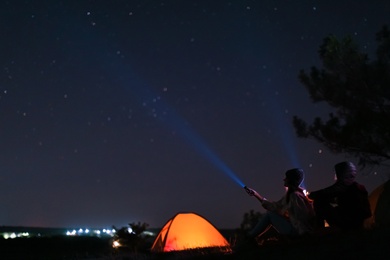 Couple with flashlights near camping tent outdoors at night