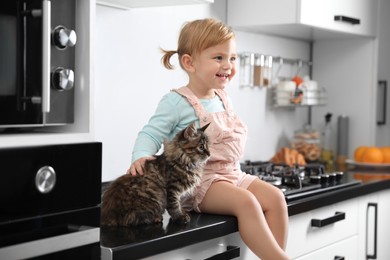 Cute little child sitting with adorable pet on countertop in kitchen