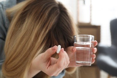 Young woman with abortion pill and water indoors, focus on hand