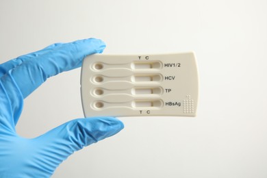 Doctor in gloves holding disposable express test for hepatitis on white background, closeup
