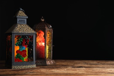 Decorative Arabic lanterns on wooden table against black background, space for text