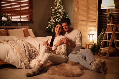 Happy couple sitting in festively decorated bedroom. Christmas celebration