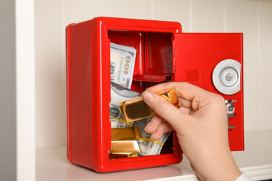 Woman putting gold bar into red steel safe, closeup
