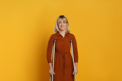 Portrait of happy woman with crutches on yellow background
