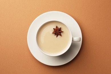 Photo of Cup of tea with milk and anise star on brown background, top view