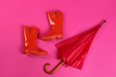 Beautiful red umbrella and rubber boots on pink background, flat lay