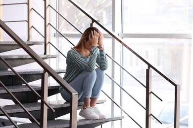 Emotional teenage girl sitting on stairs indoors