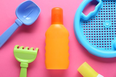 Bottle of suntan cream and children's beach toys on pink background, flat lay