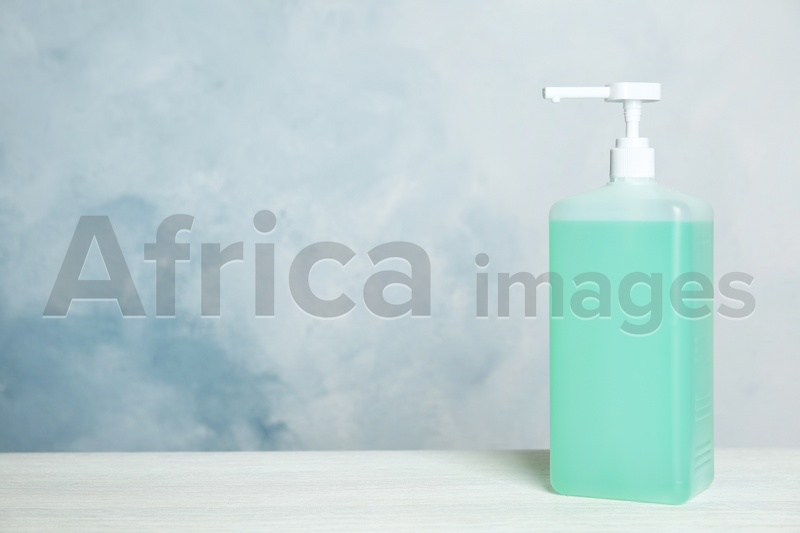 Dispenser bottle with green antiseptic gel on table against light background. Space for text