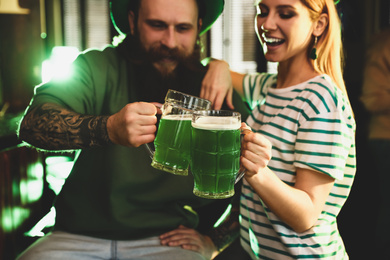 Young woman and man toasting with green beer in pub, focus on glasses. St. Patrick's Day celebration