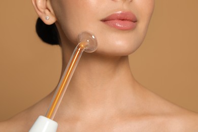 Woman using high frequency darsonval device on beige background, closeup