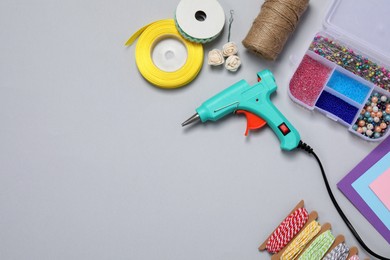 Hot glue gun and handicraft materials on grey background, flat lay. Space for text