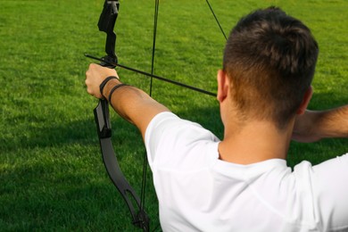 Man with bow and arrow practicing archery on green grass, back view