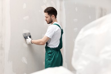 Worker in uniform plastering wall with putty knife indoors