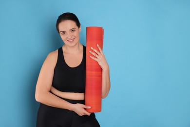 Happy overweight woman with yoga mat on light blue background. Space for text