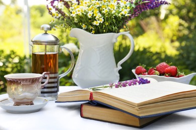 Books, tea and bouquet of beautiful wildflowers on table in garden