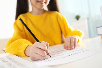 Little girl writing music notes at table, closeup