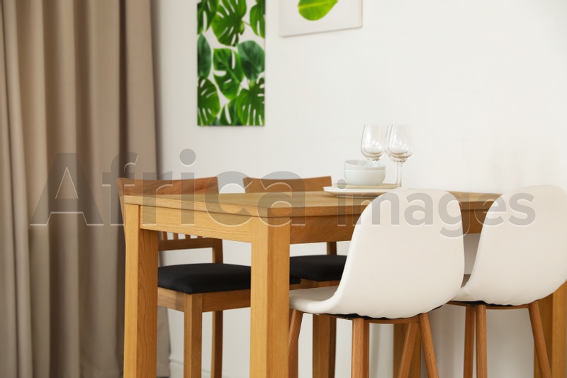 Stylish room interior with dining table and bar stools near white wall