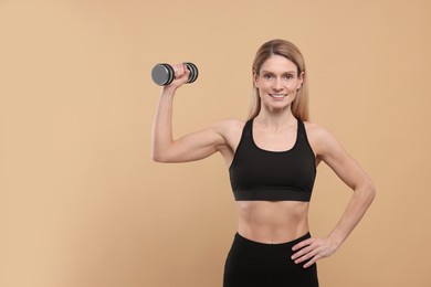 Photo of Athletic woman exercising with dumbbell on beige background, space for text
