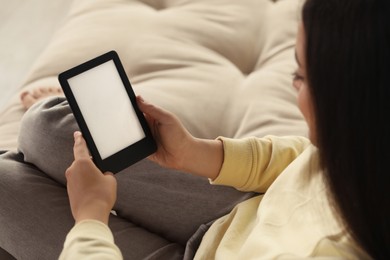 Young woman using e-book reader on sofa, closeup