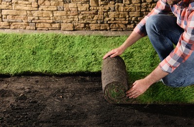Photo of Young man laying grass sod on ground at backyard, closeup. Space for text