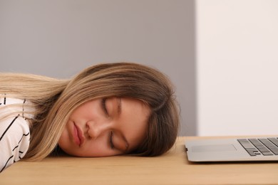 Young woman sleeping in front of laptop at wooden table indoors