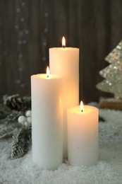 Photo of Burning candles and Christmas decor on artificial snow