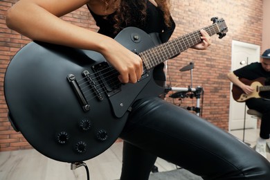 African American woman playing electric guitar during rehearsal in studio, closeup. Music band practice