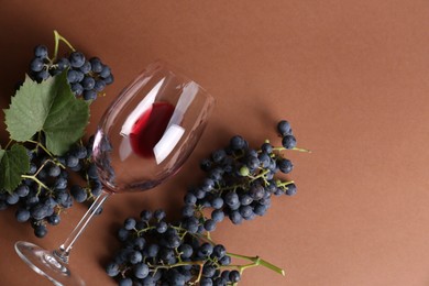 Overturned glass with red wine and grapes on brown background, flat lay. Space for text