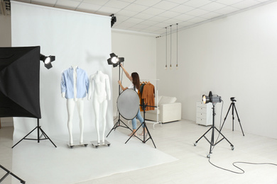Ghost mannequins with modern clothes and professional photographer fixing lighting in photo studio