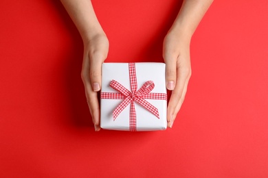 Woman holding gift box on color background, top view