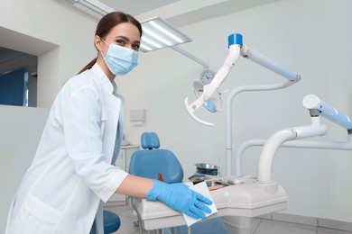 Professional dentist in white coat and medical mask cleaning workplace indoors