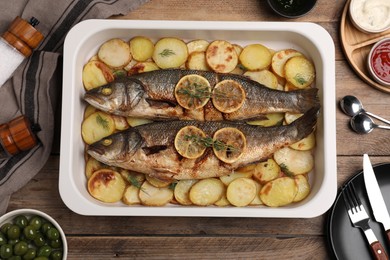 Photo of Baking tray with delicious baked sea bass fish and potatoes on wooden table, flat lay