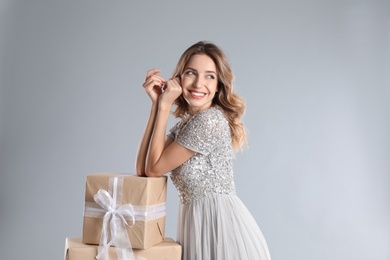 Beautiful young woman with Christmas presents on light grey background