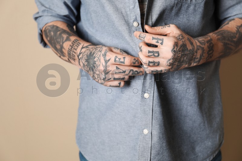 Young man with tattoos on body against beige background, closeup