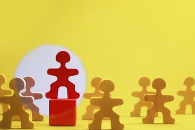 Photo of Wooden figures with red one on yellow background, space for text. Recruiter searching employee