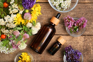 Bottles of essential oils surrounded by beautiful flowers on wooden table, flat lay