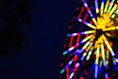 Blurred view of beautiful glowing Ferris wheel against dark sky. Space for text