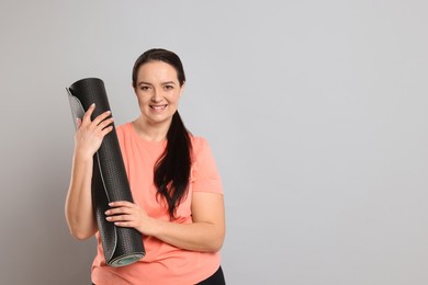 Happy overweight woman with yoga mat on grey background, space for text