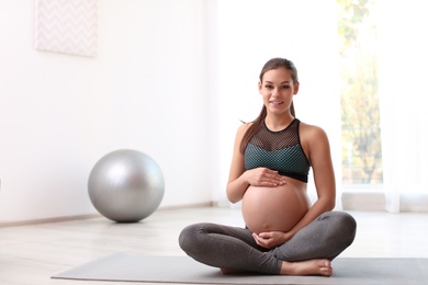 Young pregnant woman in fitness clothes at home. Space for text