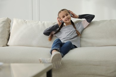 Girl with headphones sitting on comfortable sofa in living room