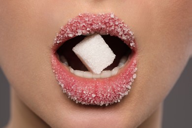 Woman with beautiful lips eating sugar cube on grey background, closeup
